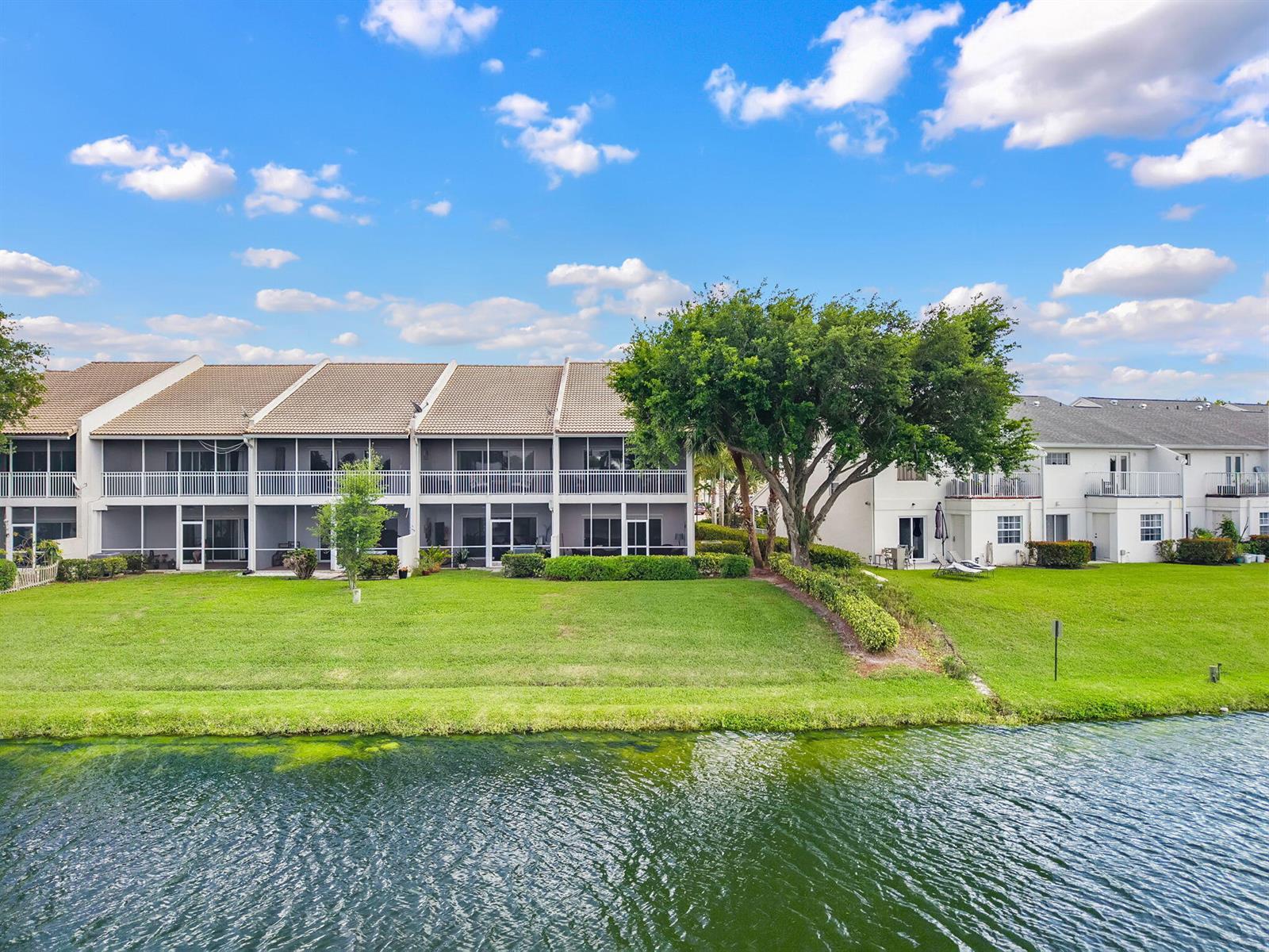 An exterior view of a multi-story townhouse complex with screened balconies overlooking a pond — 12598 Westhampton Circle, Wellington FL 33414, WELLINGTON, FL