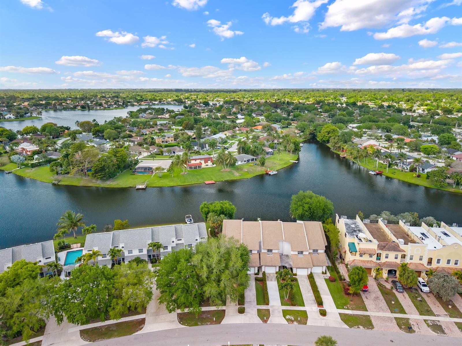 An aerial view shows townhomes along a canal with a neighborhood and trees beyond — 12598 Westhampton Circle, Wellington FL 33414, WELLINGTON, FL