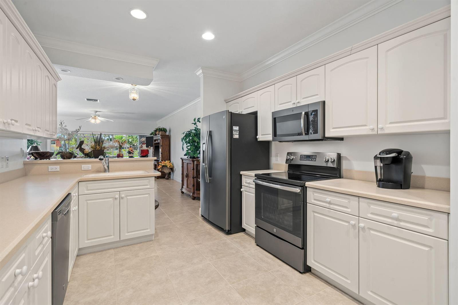 A kitchen features white cabinetry, tan countertops, and black appliances on a tiled floor — 12598 Westhampton Circle, Wellington FL 33414, WELLINGTON, FL