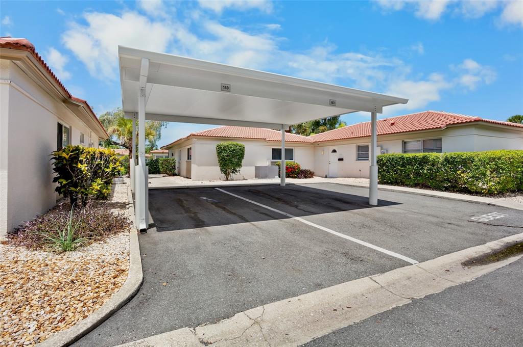 A covered carport with two parking spaces sits in front of single-story residential buildings — 159 VISTA HERMOSA CIRCLE UNIT 27B, SARASOTA, FL