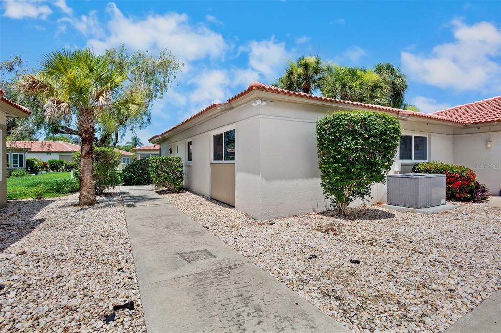 A beige house exterior with a concrete walkway, gravel landscaping, and a palm tree — 159 VISTA HERMOSA CIRCLE UNIT 27B, SARASOTA, FL