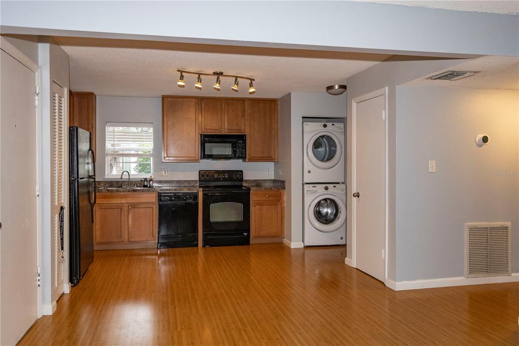 A kitchen features wood cabinets, black appliances, a stacked washer and dryer, and wood flooring — 317 E AMELIA STREET UNIT 8, ORLANDO, FL