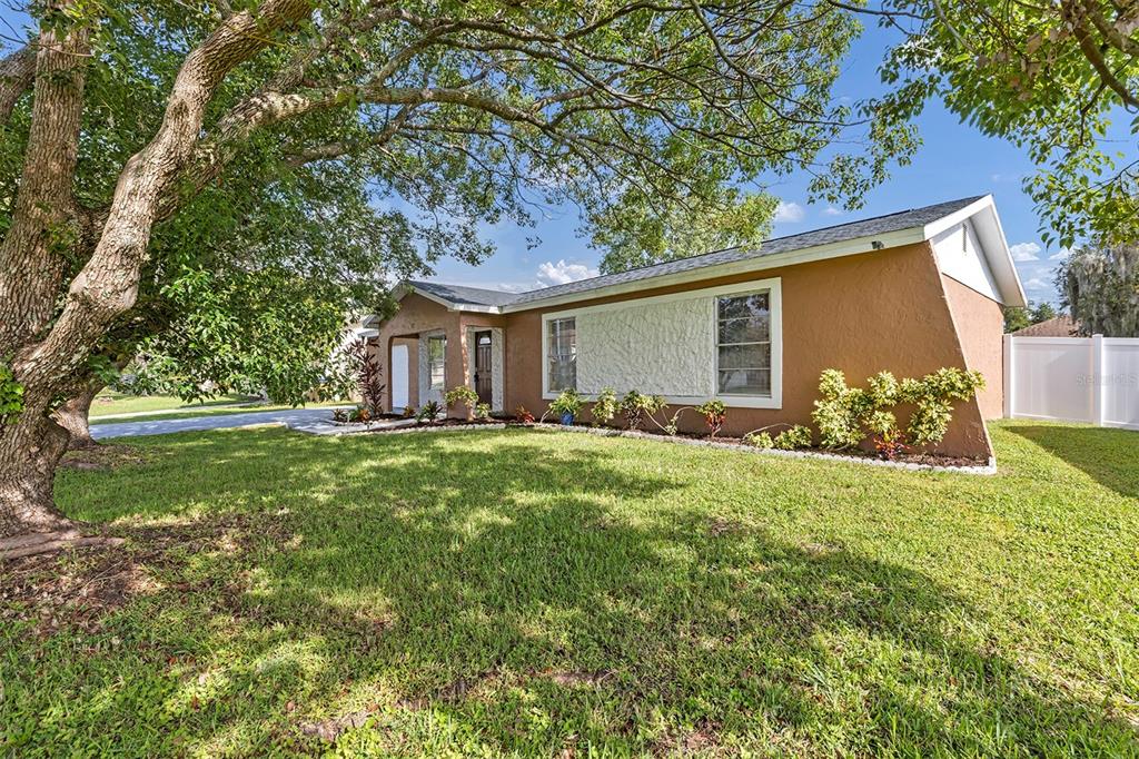 A single-story house with a tan stucco exterior, a textured white accent wall, and large trees — 819 NELSON DRIVE, KISSIMMEE, FL