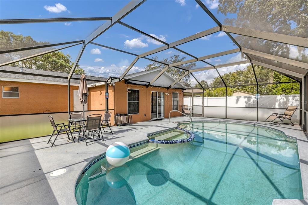 A screened-in patio features a swimming pool with a spa and outdoor dining furniture — 819 NELSON DRIVE, KISSIMMEE, FL