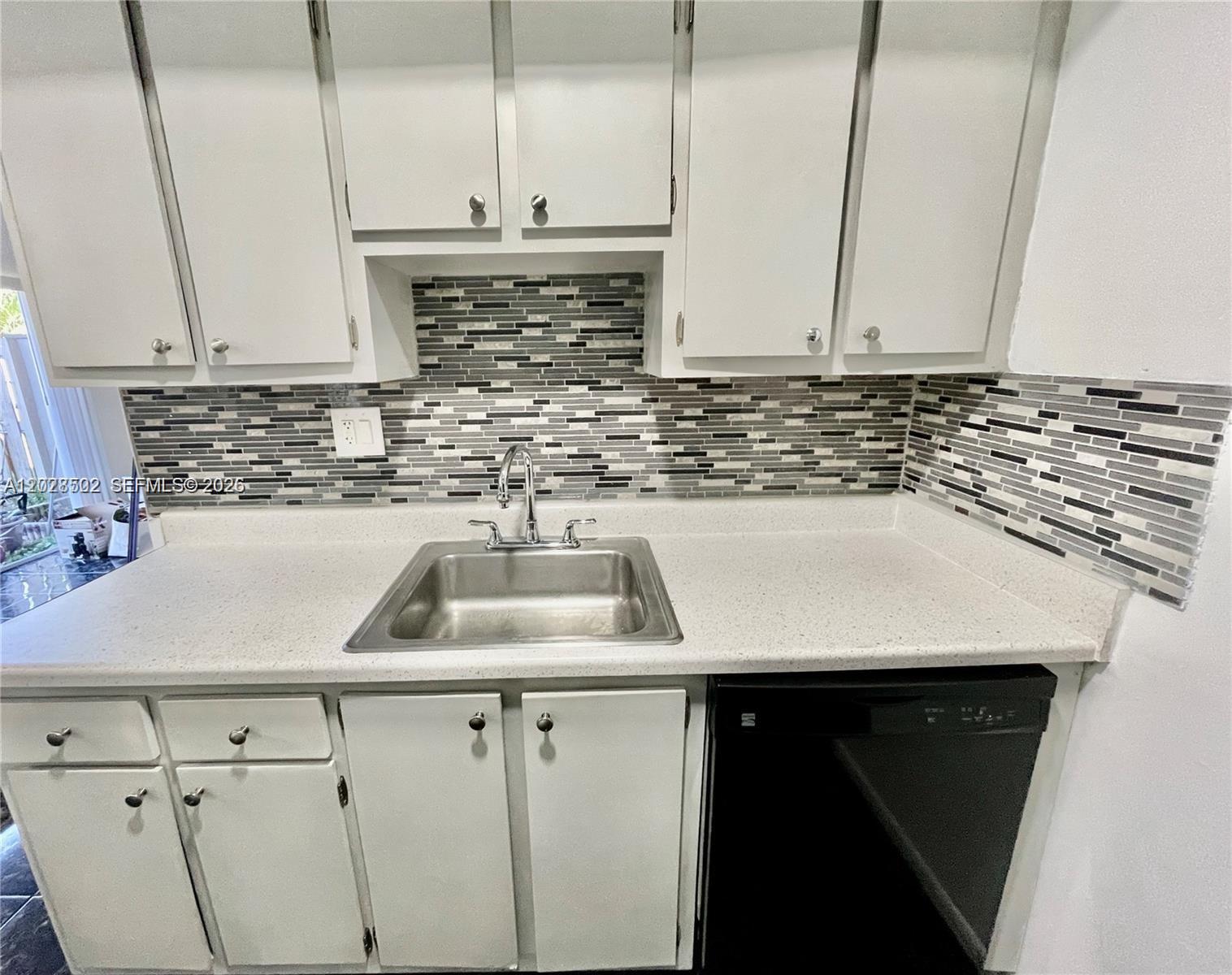 A kitchen features white cabinets, a speckled countertop, a stainless steel sink, and mosaic backsplash — 5809 NW 21st St # A, Lauderhill FL 33313, LAUDERHILL, FL