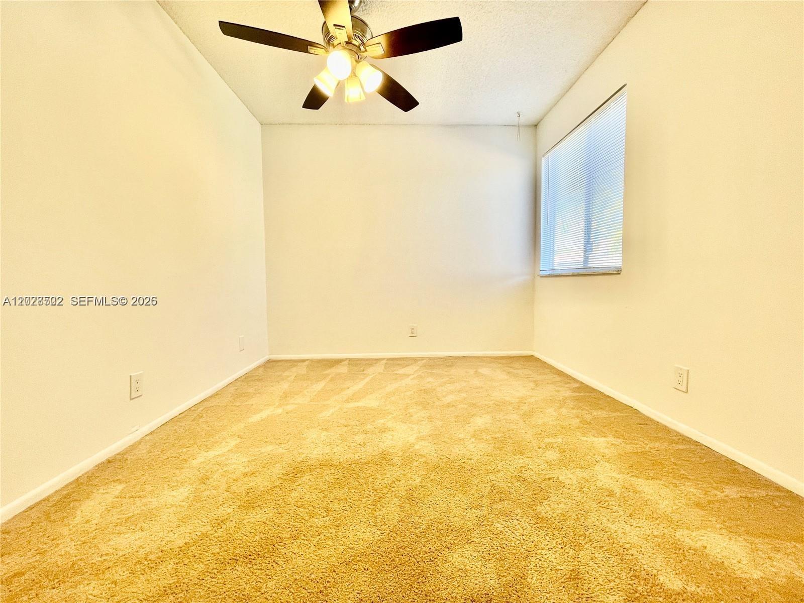 An empty room features beige carpeting, white walls, a ceiling fan, and a window — 5809 NW 21st St # A, Lauderhill FL 33313, LAUDERHILL, FL