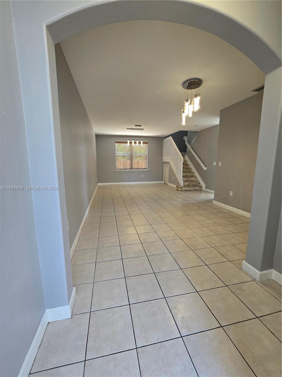 An empty room features light-colored tile flooring, gray walls, and a staircase with white railings — 5630 NW 107th Ave # 1605, Doral FL 33178, DORAL, FL
