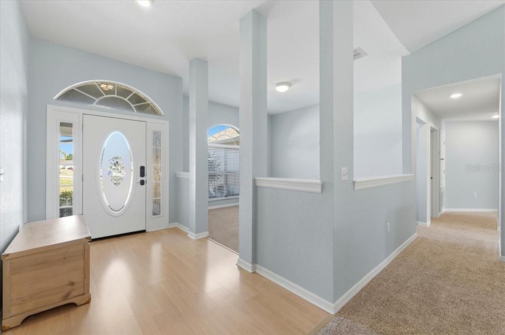 An entryway with light wood flooring, a white front door, and carpeted hallways — 6786 HIGHLANDS CREEK BOULEVARD, LAKELAND, FL