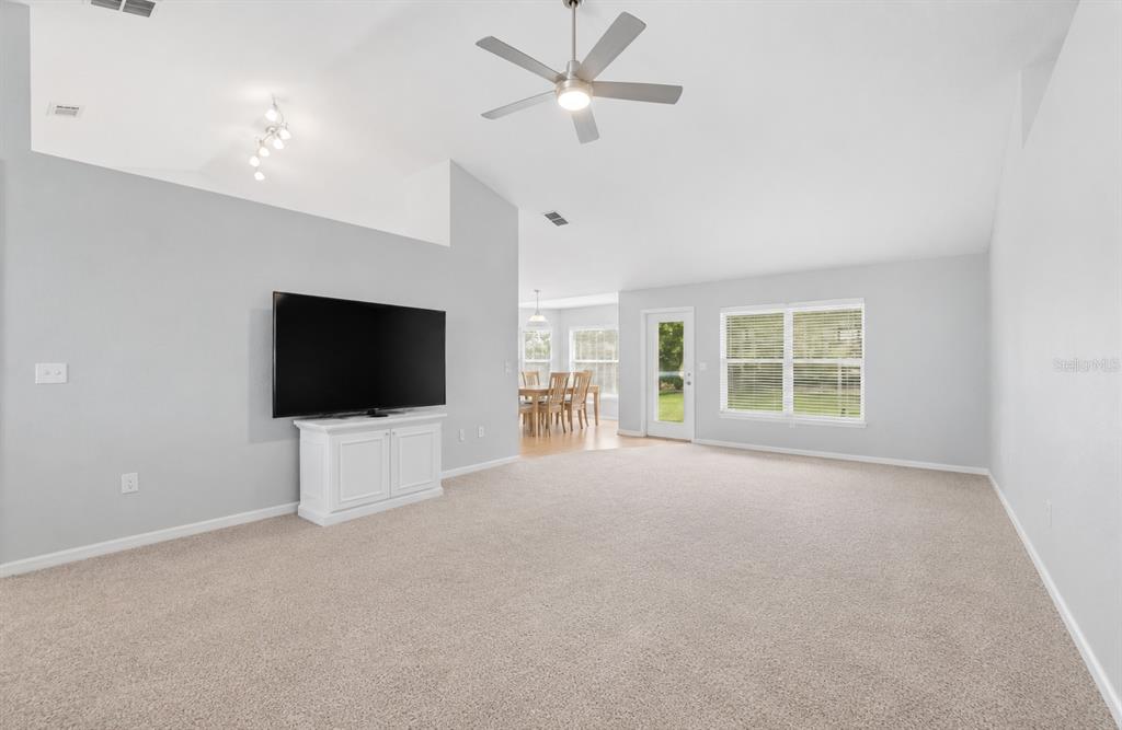 A living room with beige carpet, light gray walls, a ceiling fan, and a television — 6786 HIGHLANDS CREEK BOULEVARD, LAKELAND, FL