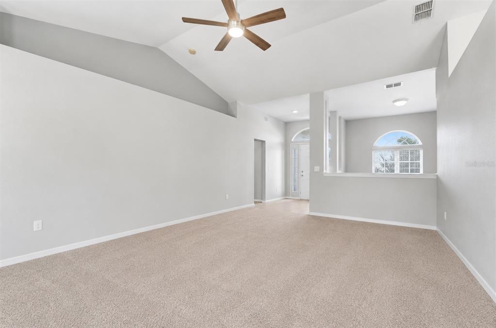 An empty living room features beige carpeting, light gray walls, and a vaulted ceiling — 6786 HIGHLANDS CREEK BOULEVARD, LAKELAND, FL
