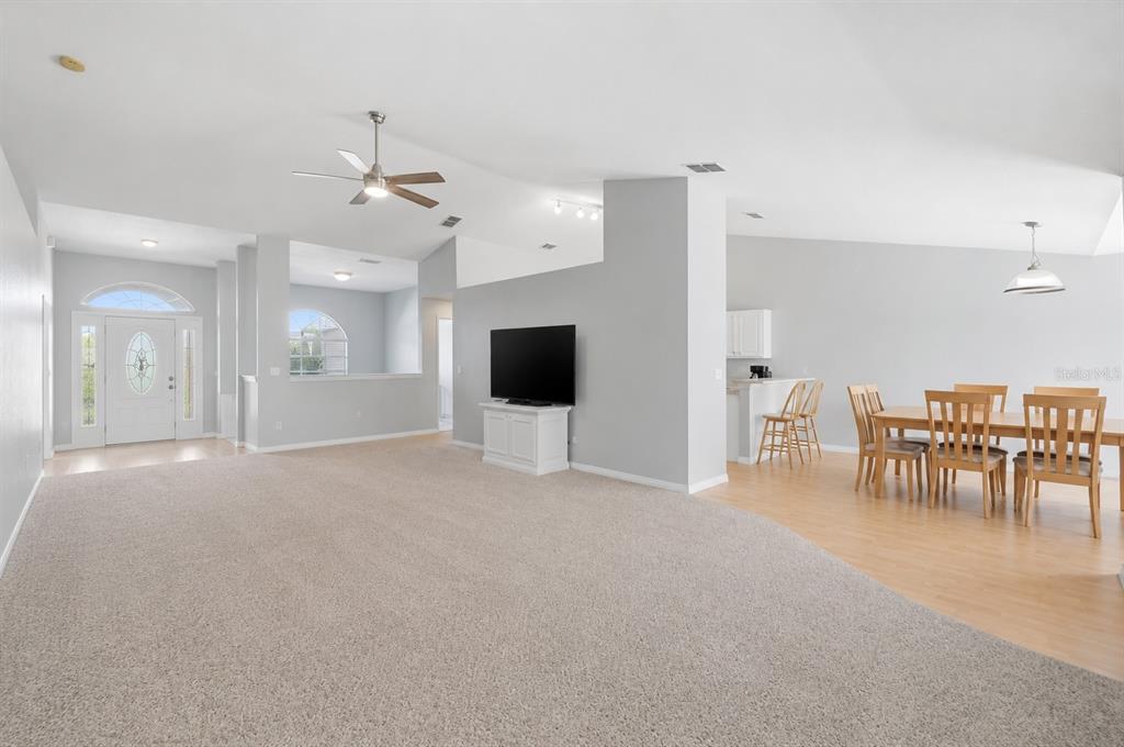A living room with carpeted floors transitions into a dining area with wood flooring — 6786 HIGHLANDS CREEK BOULEVARD, LAKELAND, FL