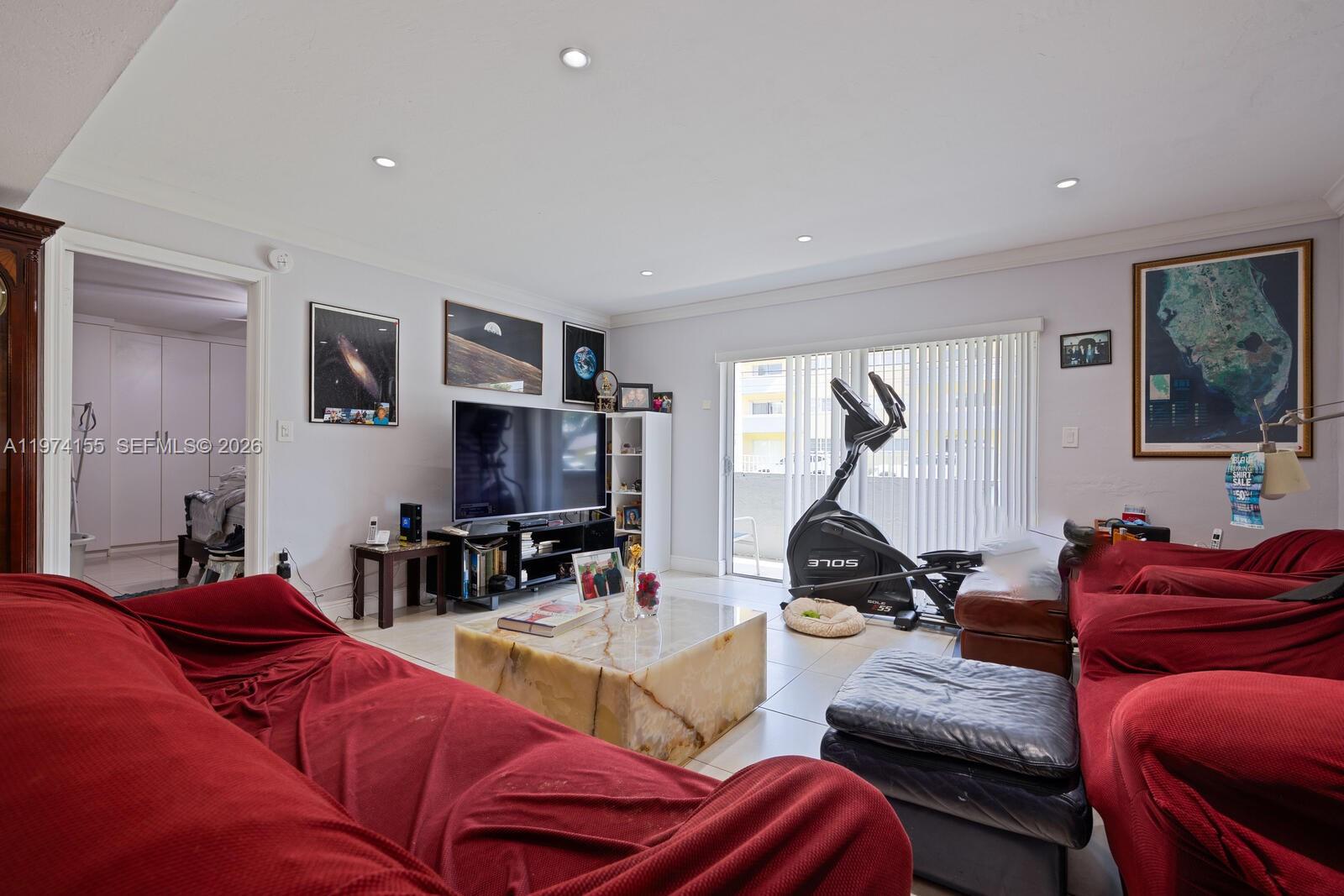 A living room features red-covered sofas, a stone coffee table, a television, and an elliptical machine — 7401 SW 82nd st # 109s, Miami FL 33143, MIAMI, FL