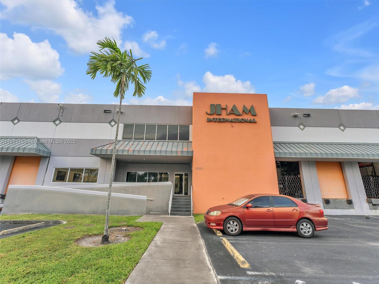 A commercial warehouse building features an orange facade with signage and a parked red sedan — 10855 NW 27th St, Doral FL 33172, DORAL, FL