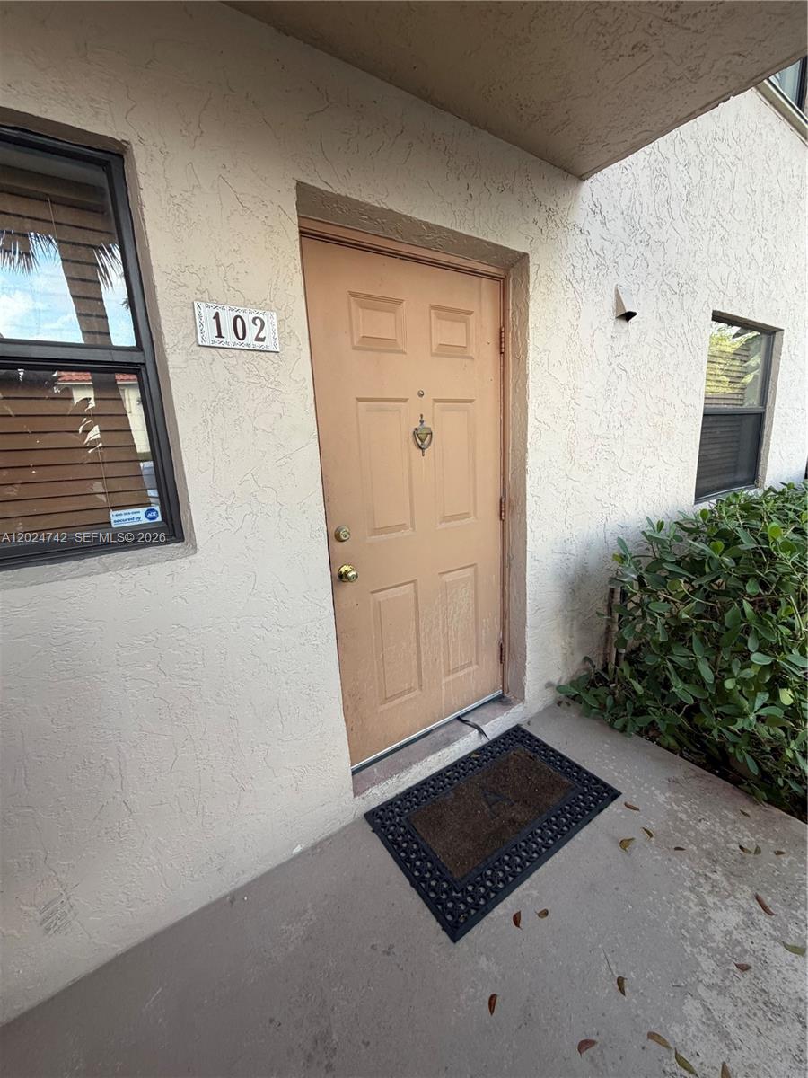 The exterior view shows a tan front door labeled 102 with a black welcome mat — 15718 E Waterside Cir # 102, Sunrise FL 33326, SUNRISE, FL