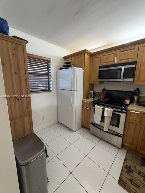 A kitchen features wood cabinets, white appliances, tiled floors, and a window with blinds — 15718 E Waterside Cir # 102, Sunrise FL 33326, SUNRISE, FL