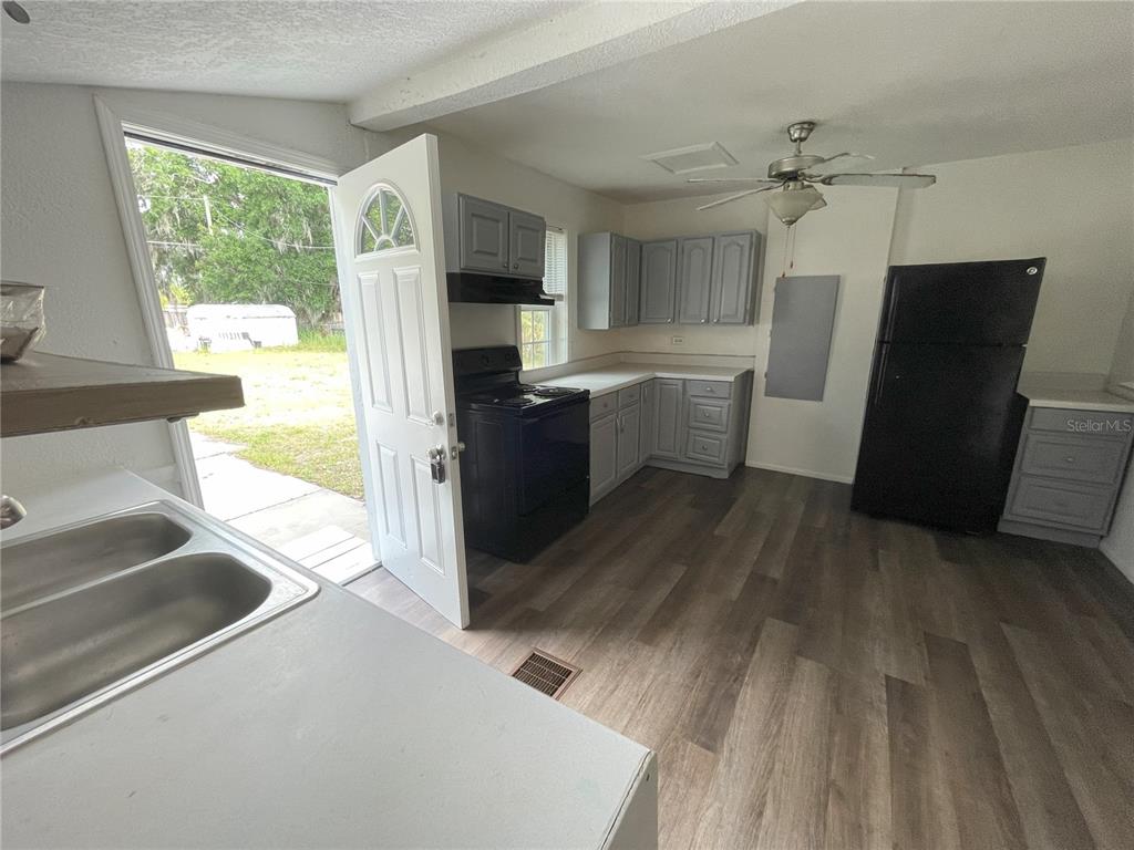 A kitchen features grey cabinets, black appliances, wood-look flooring, and an open exterior door — 1022 OREGON AVENUE, ST CLOUD, FL