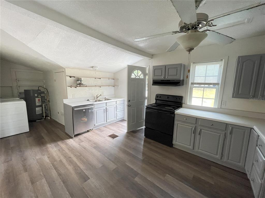 A kitchen features gray cabinets, black appliances, wood-look flooring, and an open laundry area — 1022 OREGON AVENUE, ST CLOUD, FL