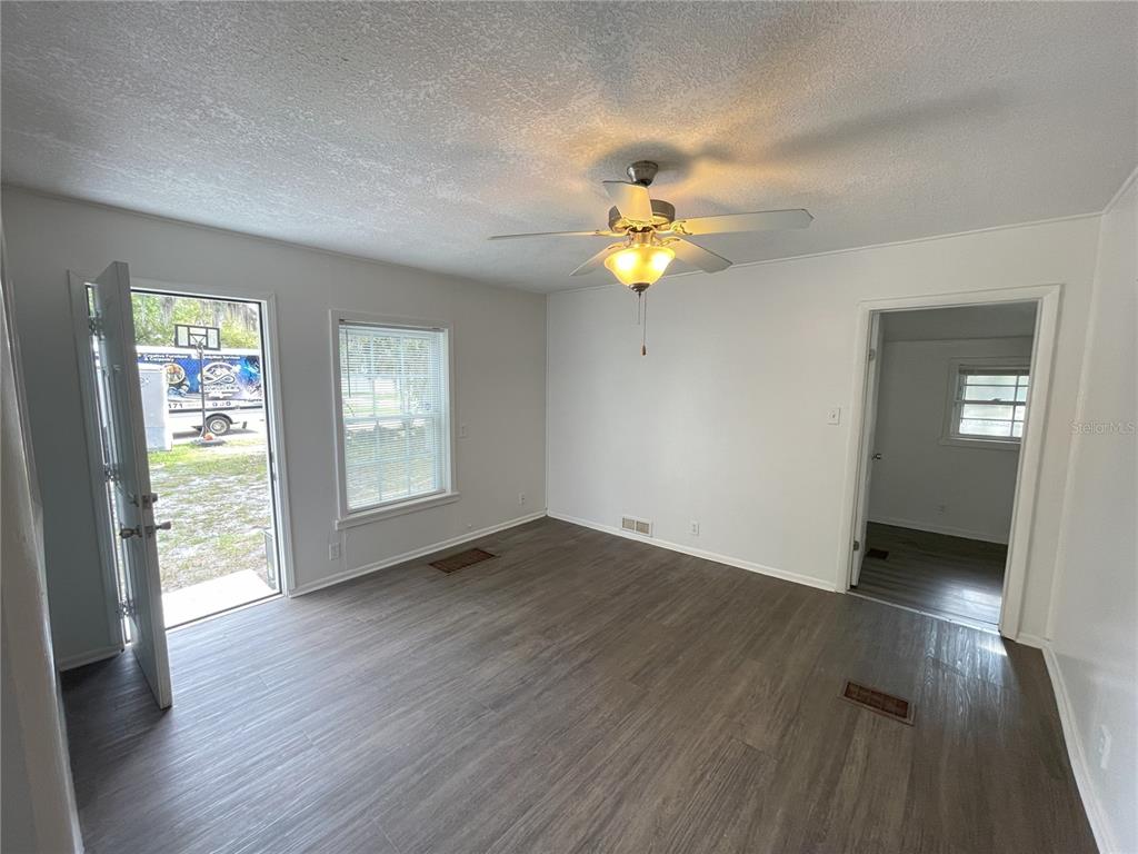 An empty room features gray wood-look flooring, white walls, a ceiling fan, and an open door — 1022 OREGON AVENUE, ST CLOUD, FL