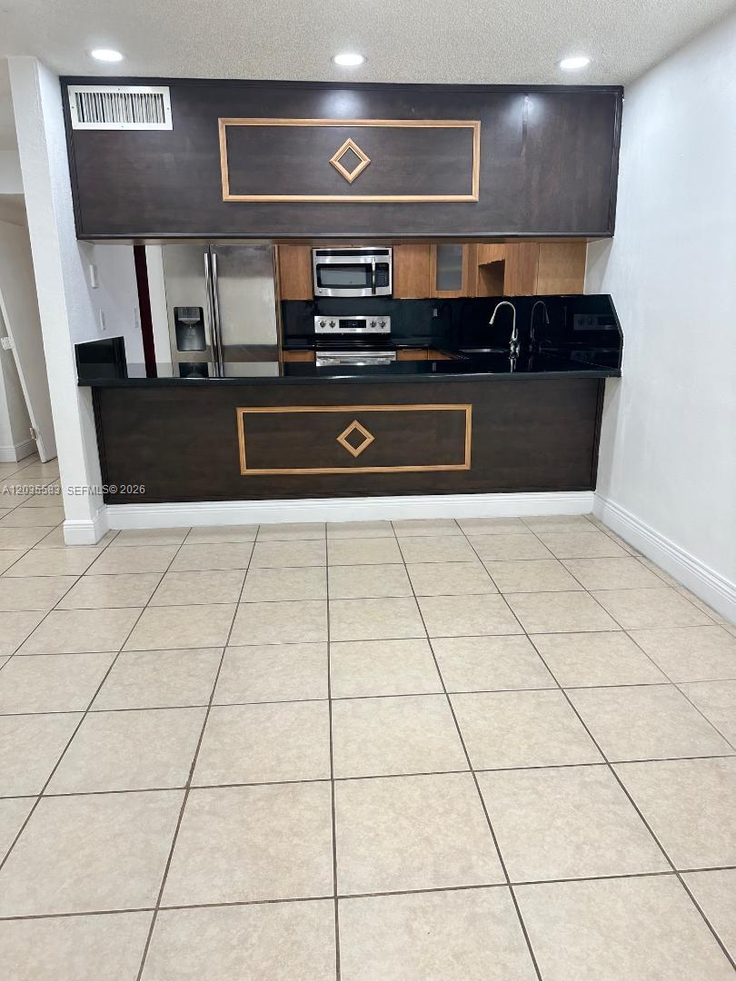 A kitchen features dark wood cabinetry, black countertops, and light-colored tiled flooring — 7205 W 3rd Ave, Hialeah FL 33014, HIALEAH, FL