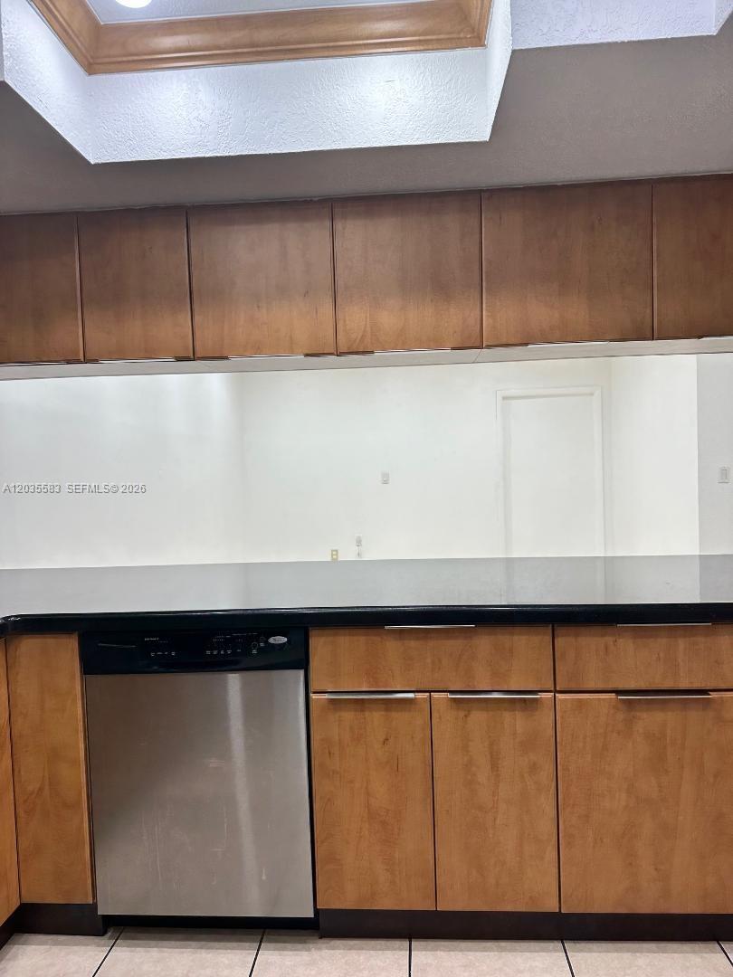 A kitchen features wood cabinets, a black countertop, and a stainless steel dishwasher — 7205 W 3rd Ave, Hialeah FL 33014, HIALEAH, FL