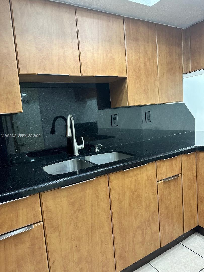 A kitchen features wood-toned cabinets, a black countertop, and a black backsplash — 7205 W 3rd Ave, Hialeah FL 33014, HIALEAH, FL