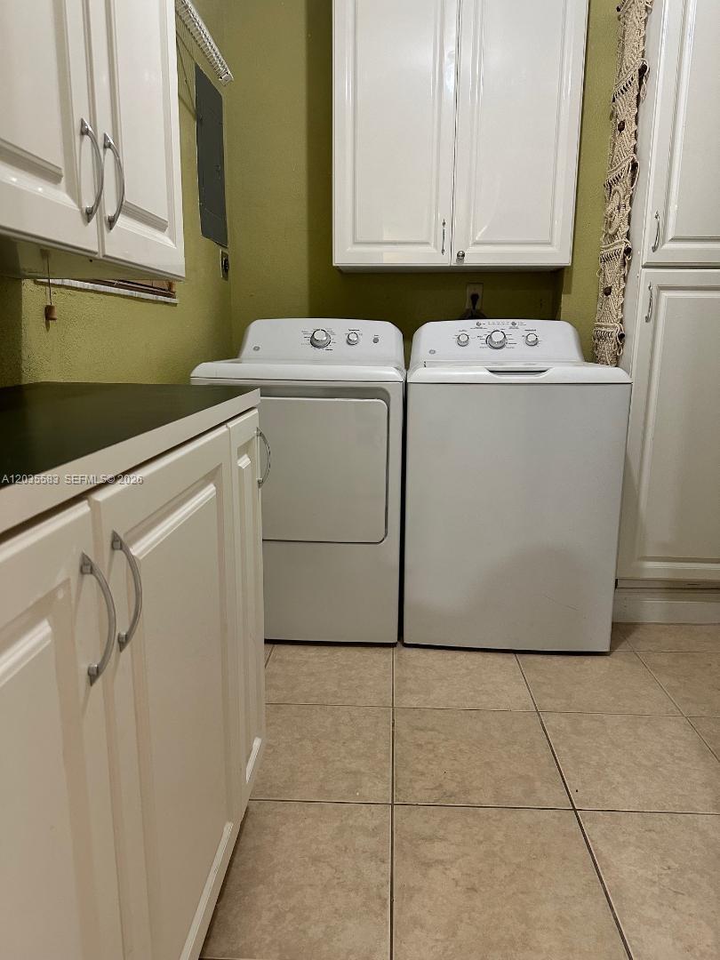 A laundry room features white cabinets, a washer, a dryer, and light-colored tile flooring — 7205 W 3rd Ave, Hialeah FL 33014, HIALEAH, FL