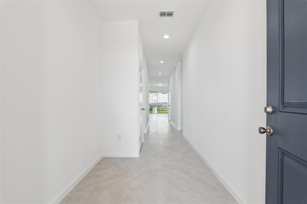 A long, white-walled hallway with light-colored tile flooring leads toward a glass sliding door — 3712 WATERCLIFF CIRCLE, GRAND ISLAND, FL