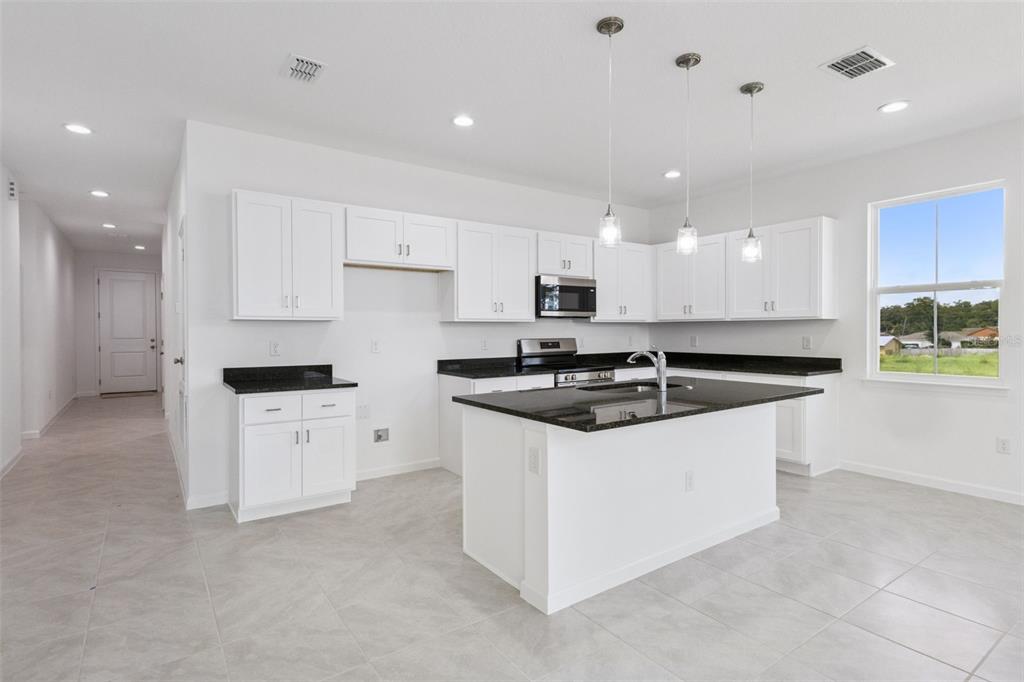 A modern kitchen features white cabinets, black countertops, a center island, and tile flooring — 3712 WATERCLIFF CIRCLE, GRAND ISLAND, FL