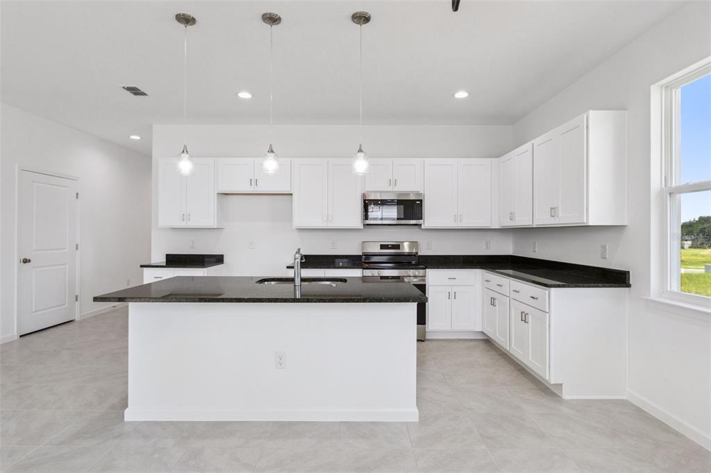 A modern kitchen features white cabinets, black countertops, a central island, and stainless steel appliances — 3712 WATERCLIFF CIRCLE, GRAND ISLAND, FL