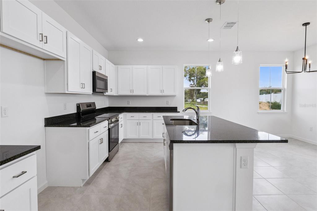 A modern kitchen features white cabinets, black granite countertops, a center island, and tile flooring — 3712 WATERCLIFF CIRCLE, GRAND ISLAND, FL