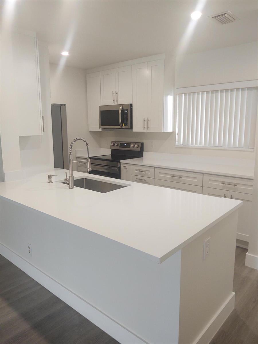 A modern kitchen features white cabinets, a large island with a sink, and stainless appliances — 140 NW 70th # 2040, Boca Raton FL 33487, BOCA RATON, FL