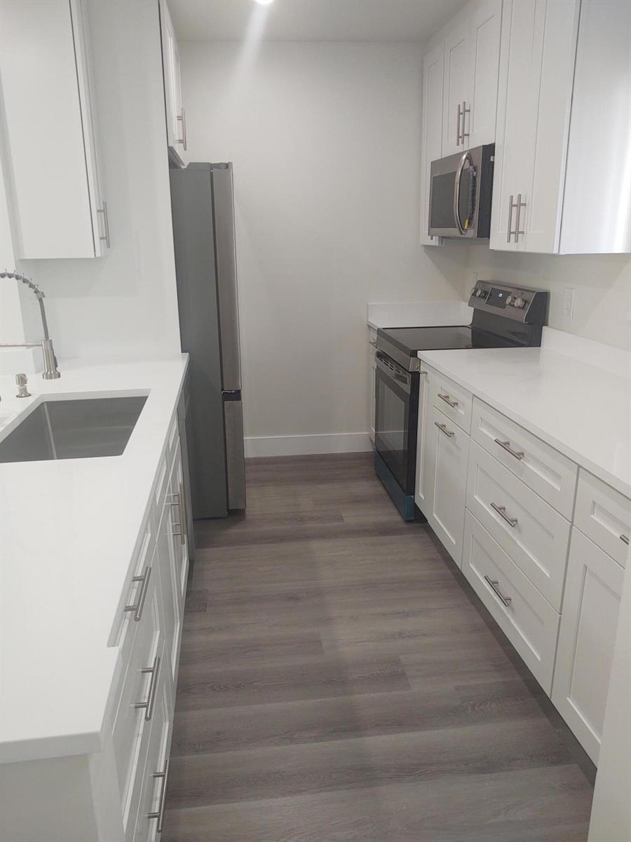 A galley kitchen features white cabinets, stainless steel appliances, and gray wood-look flooring — 140 NW 70th # 2040, Boca Raton FL 33487, BOCA RATON, FL