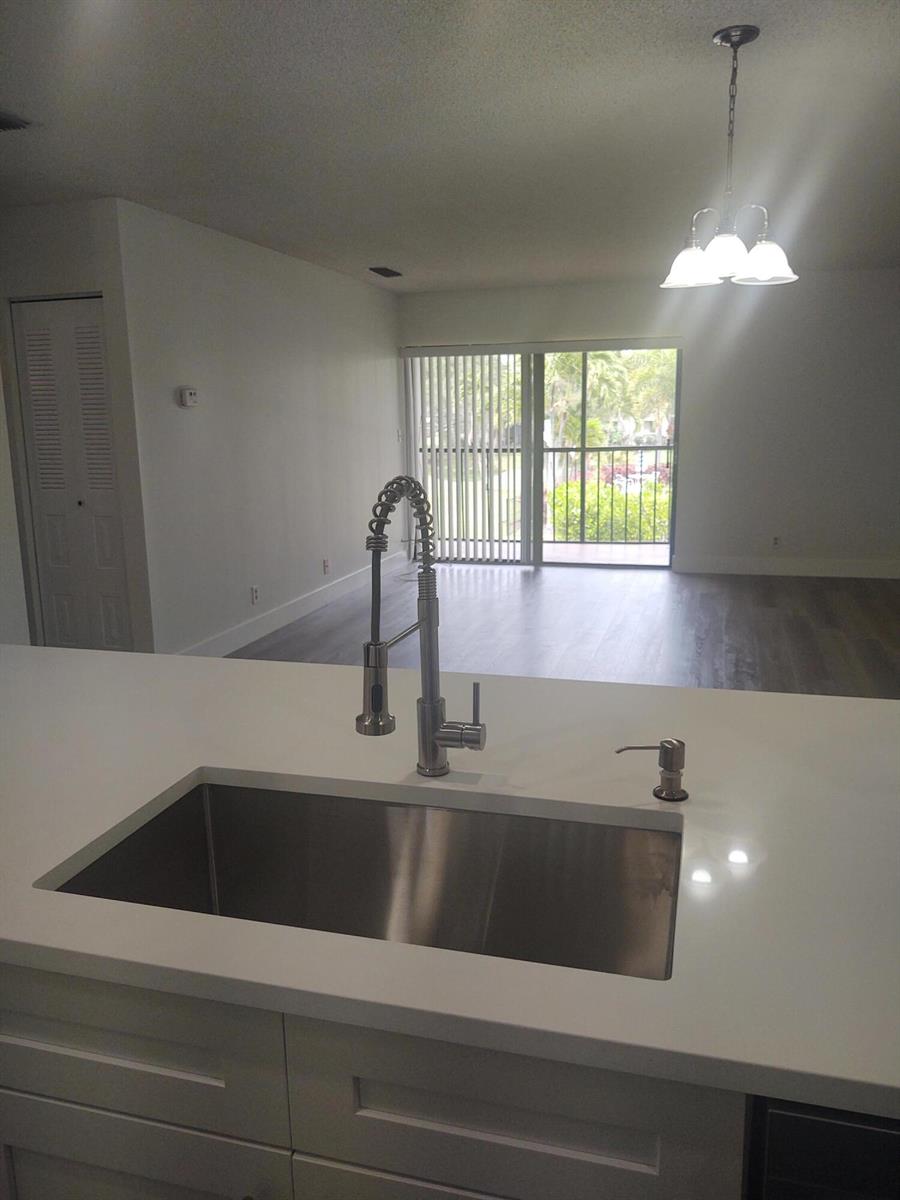 A kitchen sink with a modern faucet overlooks an open living area with sliding doors — 140 NW 70th # 2040, Boca Raton FL 33487, BOCA RATON, FL