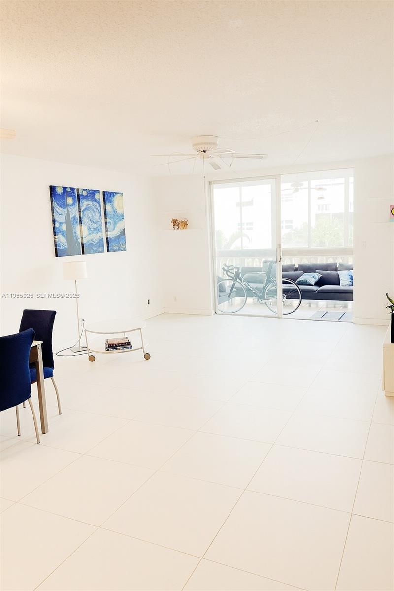 A bright living room features white tile floors, a ceiling fan, and a sliding glass door — 610 NE 12th Ave # 308, Hallandale Beach FL 33009, HALLANDALE BEACH, FL