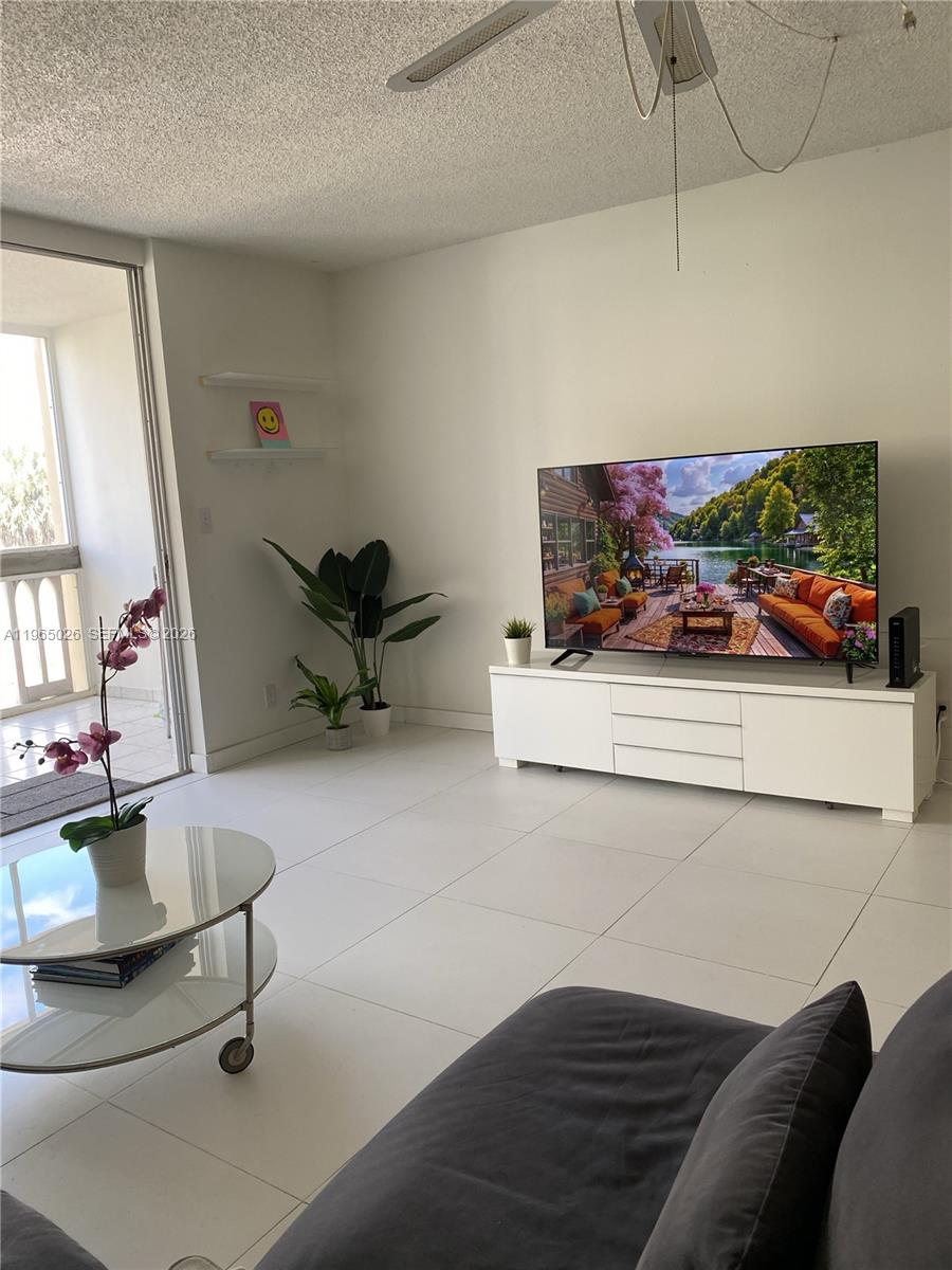 A living room features white tile floors, a white media console, and a balcony door — 610 NE 12th Ave # 308, Hallandale Beach FL 33009, HALLANDALE BEACH, FL