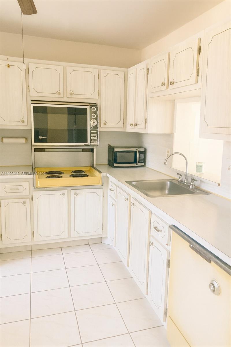 A kitchen features white cabinets, a yellow stovetop, a stainless steel sink, and tile flooring — 610 NE 12th Ave # 308, Hallandale Beach FL 33009, HALLANDALE BEACH, FL