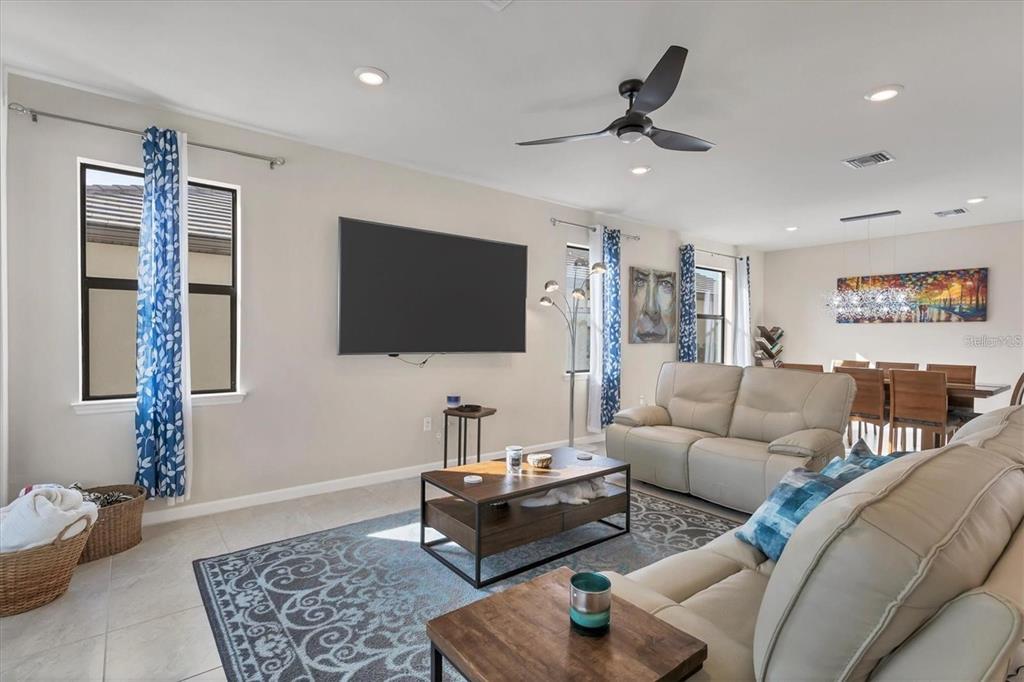 A living room features a wall-mounted television, beige leather sofas, and a patterned area rug — 5721 SWEET LEAF WAY, SARASOTA, FL
