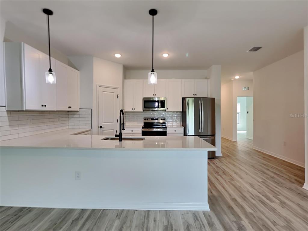 A modern kitchen features white cabinets, stainless steel appliances, a quartz island, and wood-look flooring — 1320 RIO DE JANEIRO AVENUE, PUNTA GORDA, FL