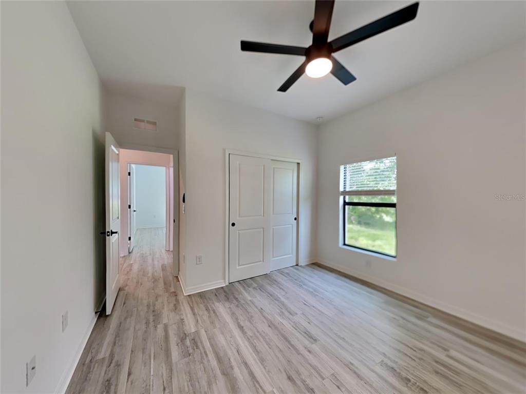 A bedroom features light wood-look flooring, white walls, a ceiling fan, and a closet — 1320 RIO DE JANEIRO AVENUE, PUNTA GORDA, FL