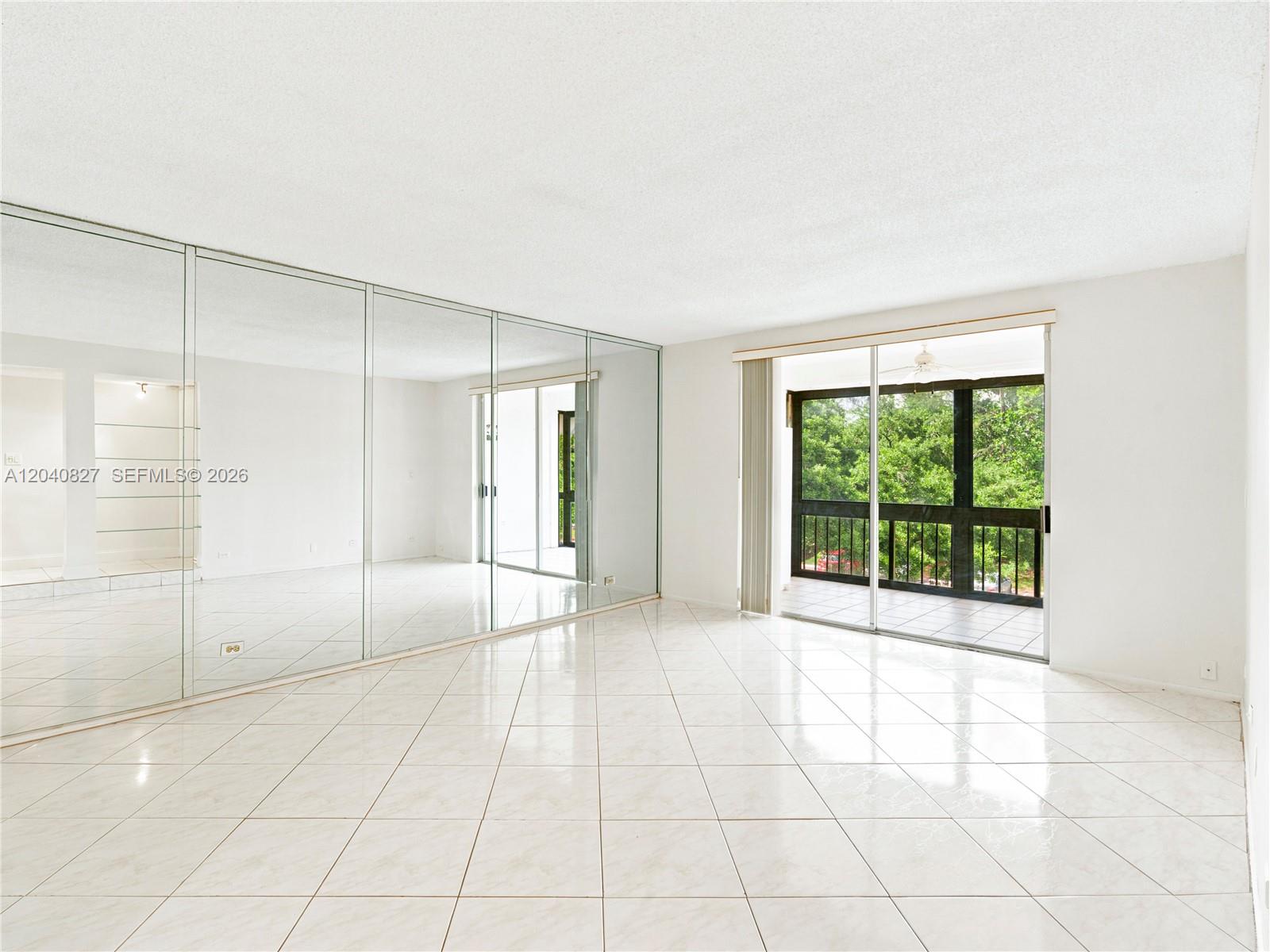 A bright room features white tile flooring, a large mirrored wall, and a sliding glass door — 3740 Inverrary Dr # 3N, Lauderhill FL 33319, LAUDERHILL, FL