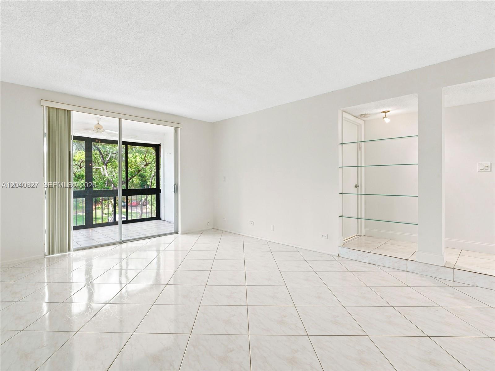 An empty room features white tiled floors, a glass sliding door, and built-in glass shelves — 3740 Inverrary Dr # 3N, Lauderhill FL 33319, LAUDERHILL, FL