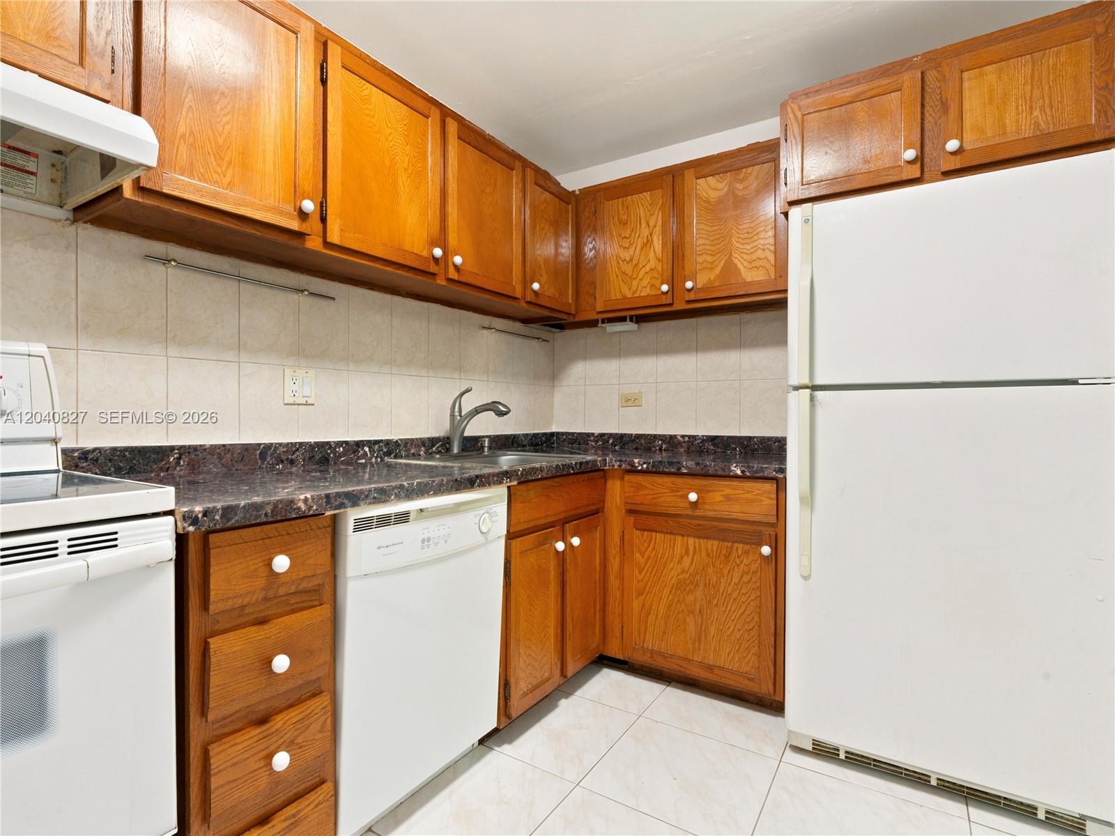 A kitchen features wood cabinets, dark laminate countertops, white appliances, and light-colored tile flooring — 3740 Inverrary Dr # 3N, Lauderhill FL 33319, LAUDERHILL, FL