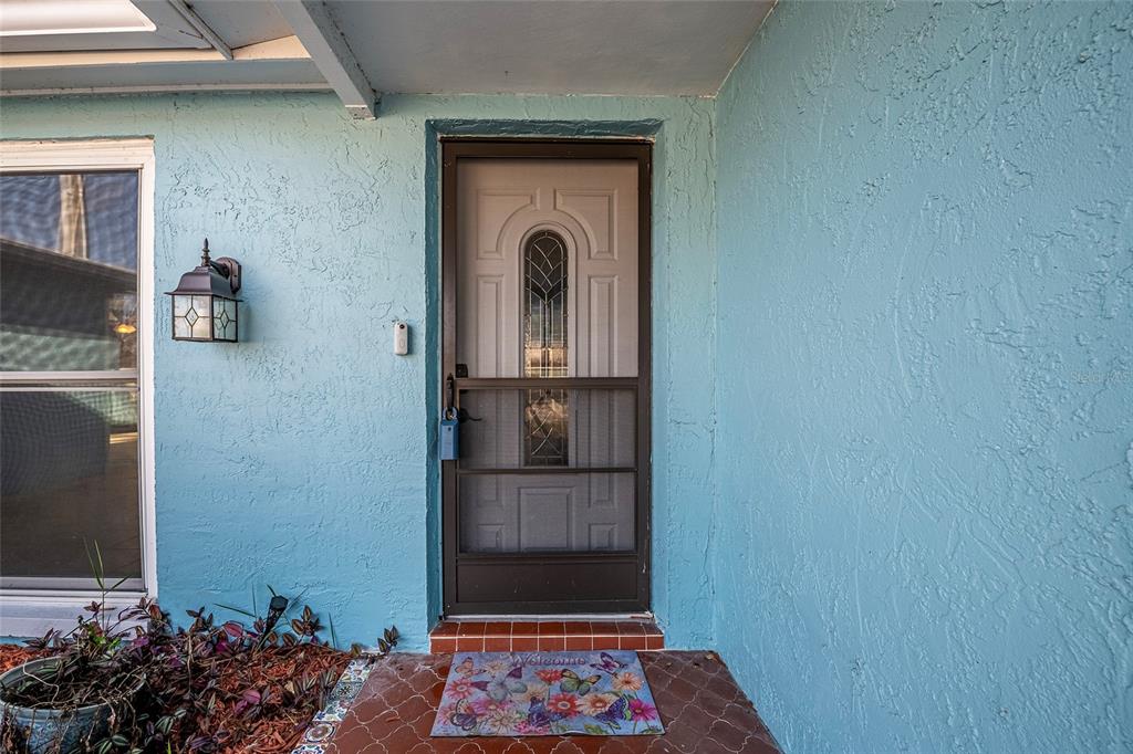 A light blue exterior wall features a front door with a screen and a doormat — 9720 GRAY FOX LANE, PORT RICHEY, FL