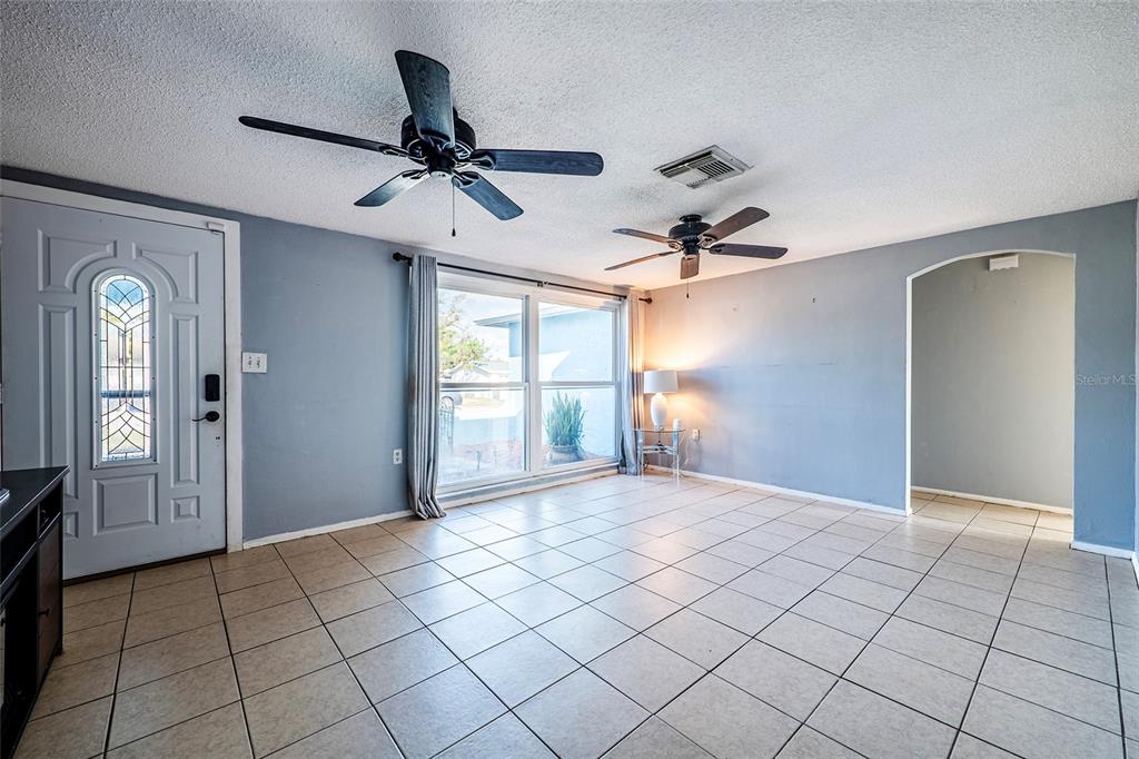 A living room with light blue walls, tiled floors, and two ceiling fans — 9720 GRAY FOX LANE, PORT RICHEY, FL