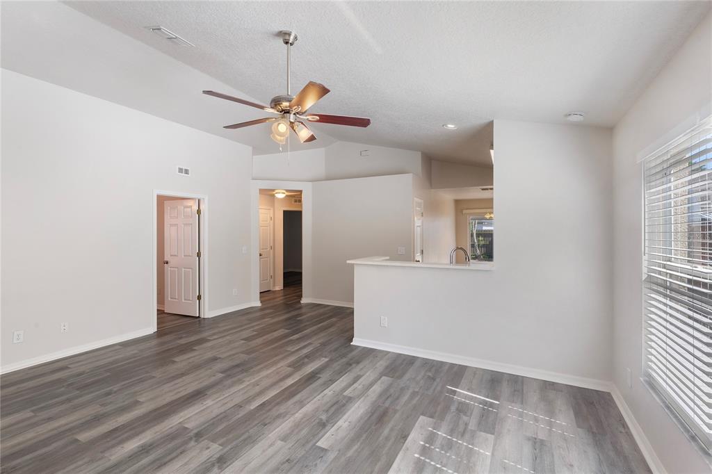 A living room with gray wood-look flooring, a ceiling fan, and a kitchen pass-through window — 7456 OXFORD GARDEN CIRCLE, APOLLO BEACH, FL