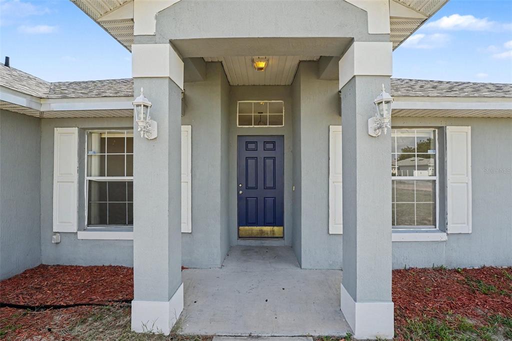 The exterior of a house features a blue front door, two windows with shutters, and columns — 1714 PILCHARD DRIVE, POINCIANA, FL