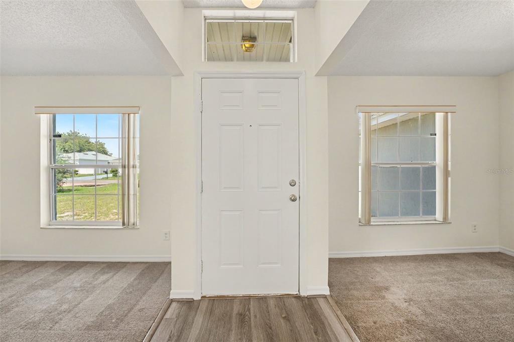 An entryway features a white front door, a transom window, and carpeted flanking rooms — 1714 PILCHARD DRIVE, POINCIANA, FL