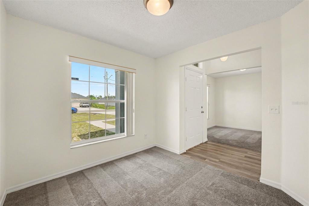A carpeted room with a window overlooks a street, leading to an entryway with flooring — 1714 PILCHARD DRIVE, POINCIANA, FL