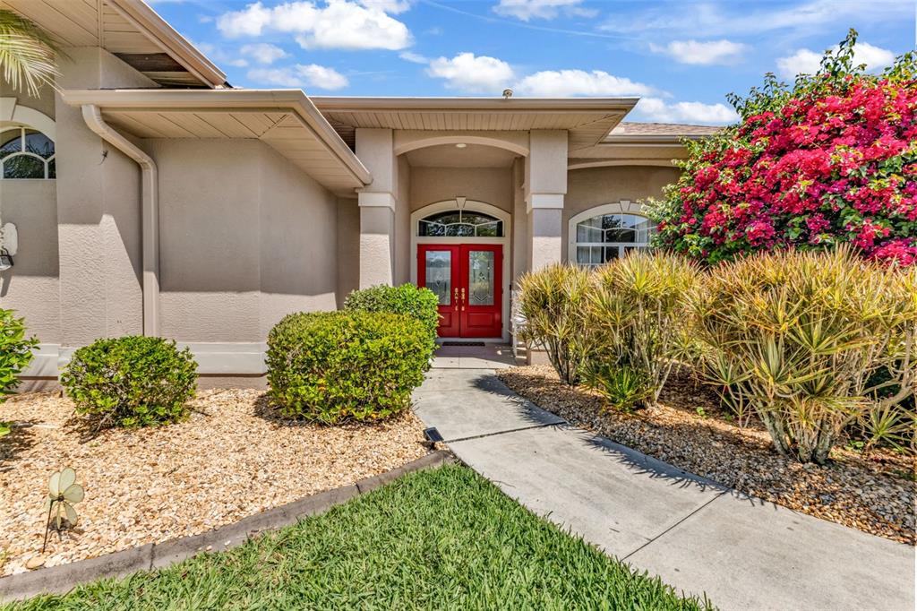 A beige house exterior features a red double front door and a concrete walkway — 25042 BOLIVAR DRIVE, PUNTA GORDA, FL