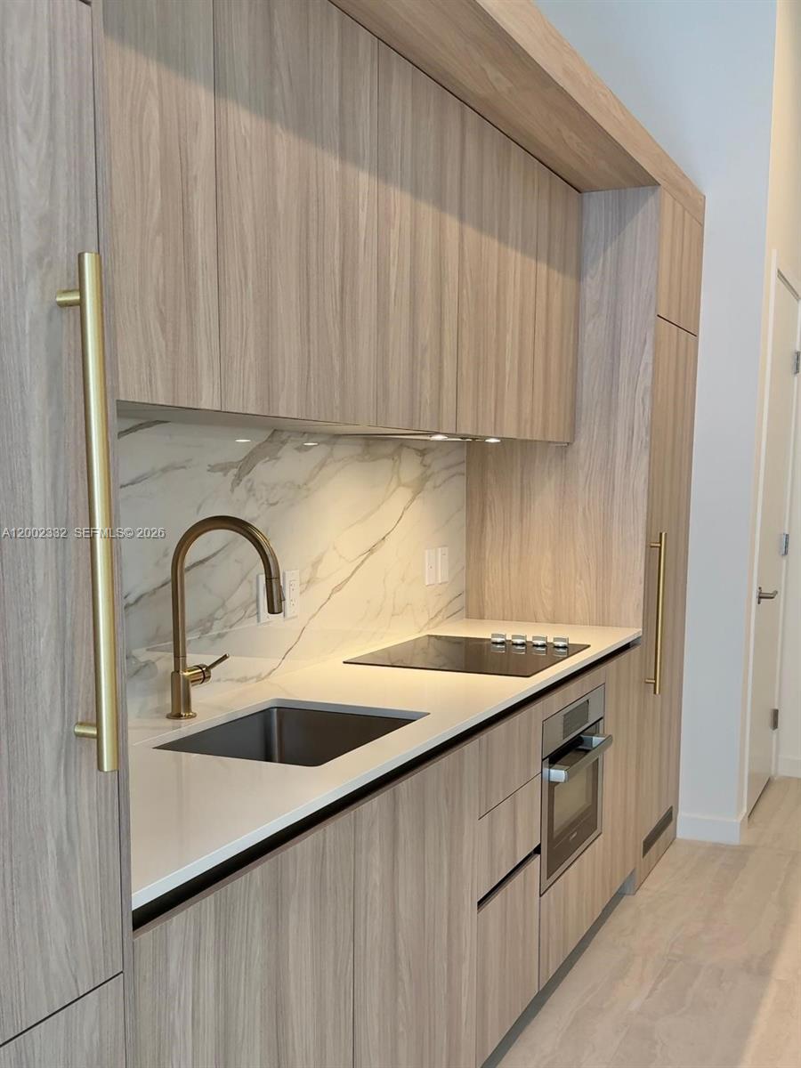 A modern kitchen features light wood cabinetry, a marble backsplash, and gold hardware — 77 SE 5th street # 1010, Miami FL 33131, MIAMI, FL